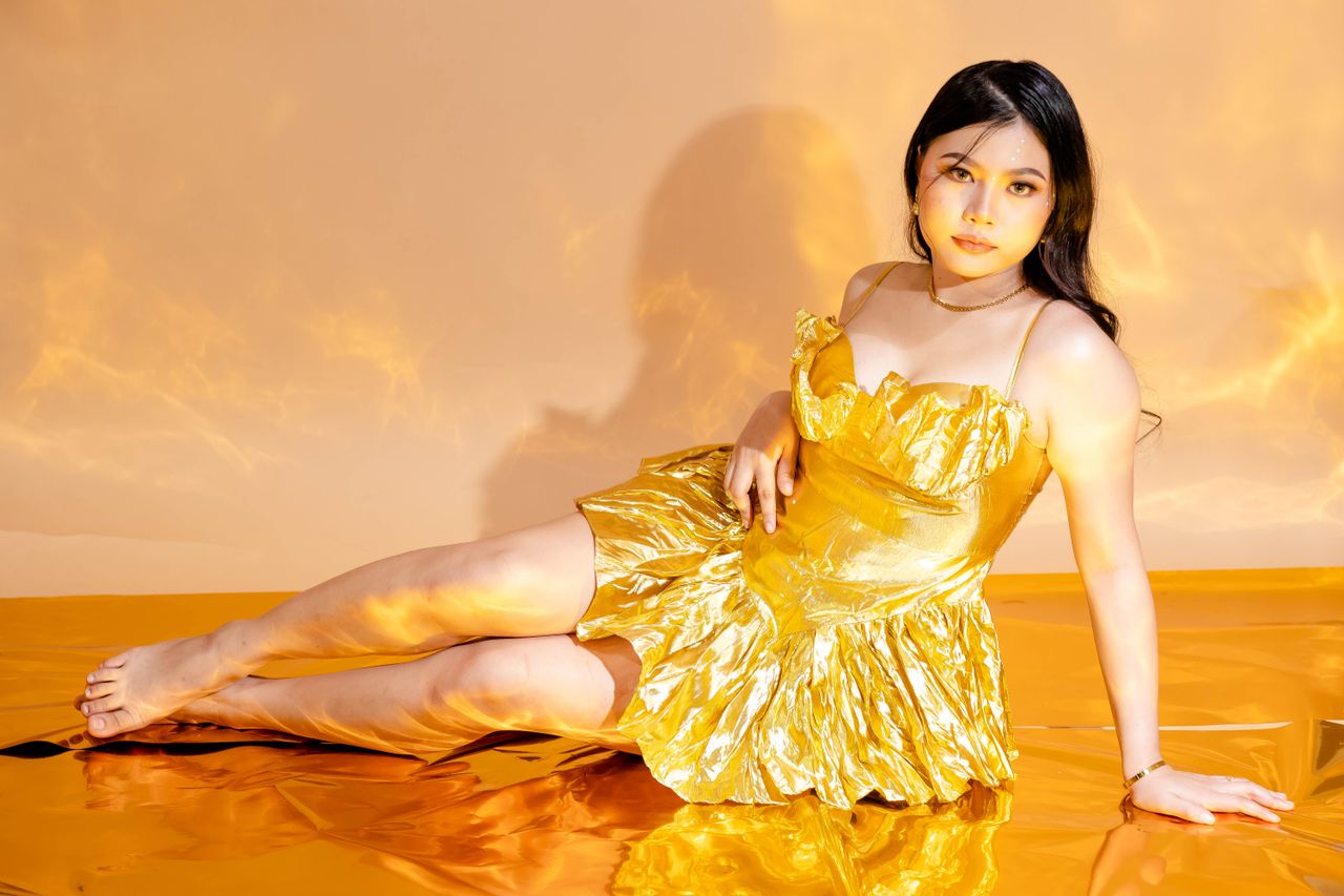 A woman in a shimmering yellow dress poses gracefully against a matching backdrop.